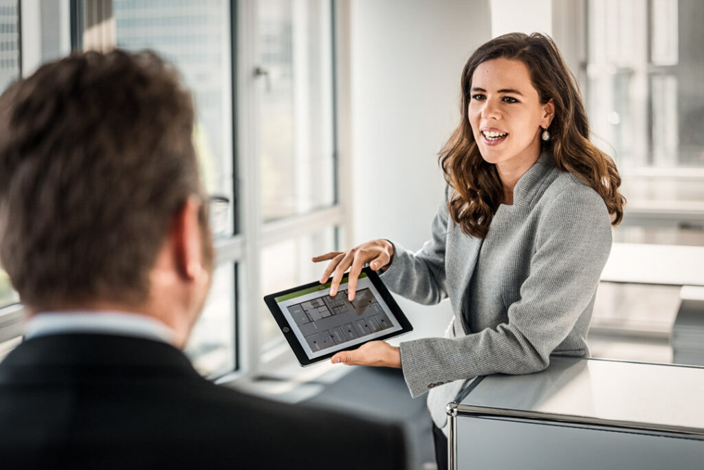 Businessmeeting in der Munich Re: Eine weibliche Kollegin zeigt einem Kollegen Inhalte auf ihrem iPad – authentische Businessfotografie.