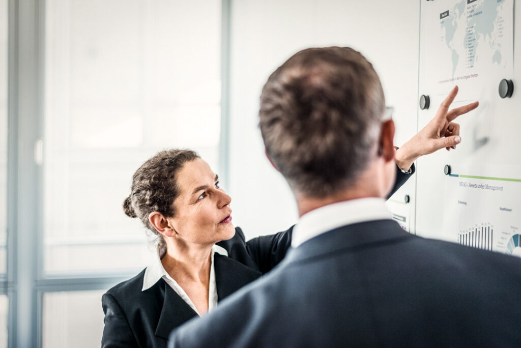 Businessfrau erklärt einem Kollegen Inhalte an einer Magnettafel im Office der MEAG AG – Businessfotograf zeigt authentische Arbeitsatmosphäre.