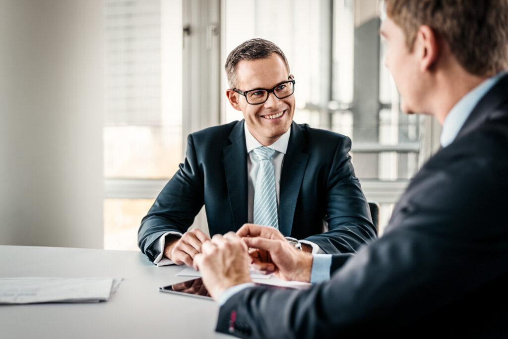 Zwei Businessmen führen ein fröhliches Meeting im Office der MEAG AG – Businessfotografie, die dynamische Zusammenarbeit in einem modernen Büro zeigt.