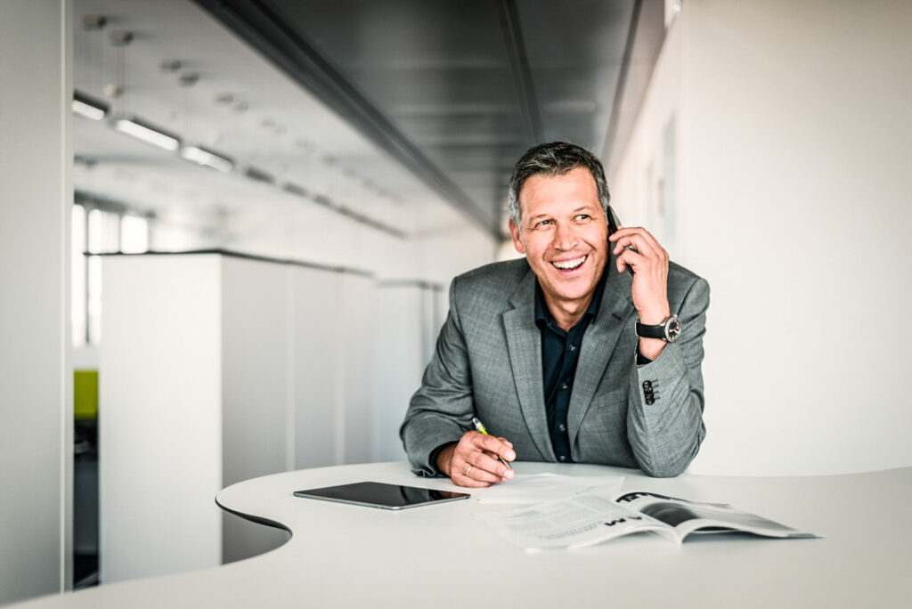 Abteilungsleiter im Anzug telefoniert konzentriert an einem Stehtisch im modernen Büro – authentische Szene, wie sie ein erfahrener businessfotograf für die MEAG AG festhält.
