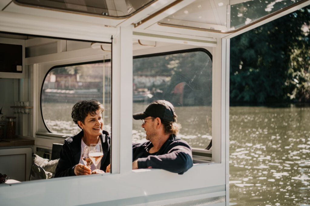 Marion Hanisch und Roland Delater, CEOs von Rollyboat, machen eine Testfahrt und lachen sich in der Kajüte des Hausboots an, Unternehmensfotografie