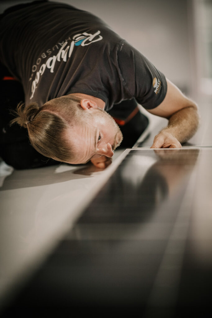Mitarbeiter überprüft mit prüfendem Blick die montierte Solarzelle auf einem Rollyboat-Hausboot, Unternehmensfotografie