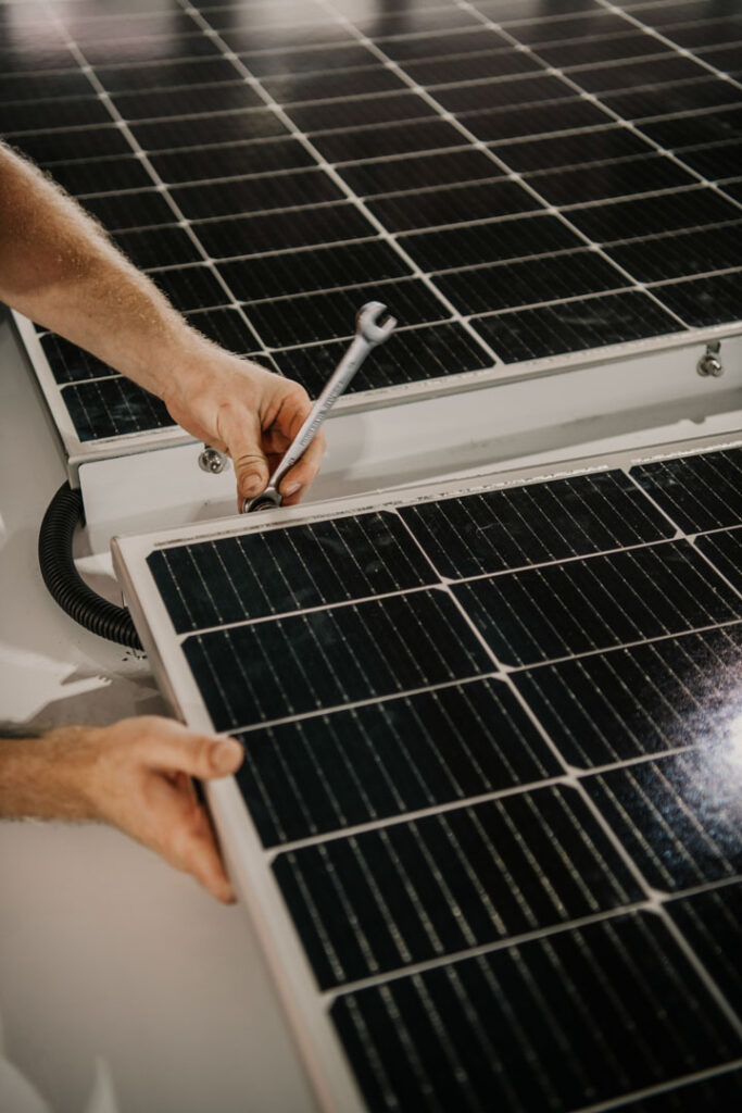 Detailaufnahme der Hände eines Mitarbeiters, der eine Solarzelle mit Schraubenschlüssel auf einem Rollyboat-Hausboot montiert, Unternehmensfotografie