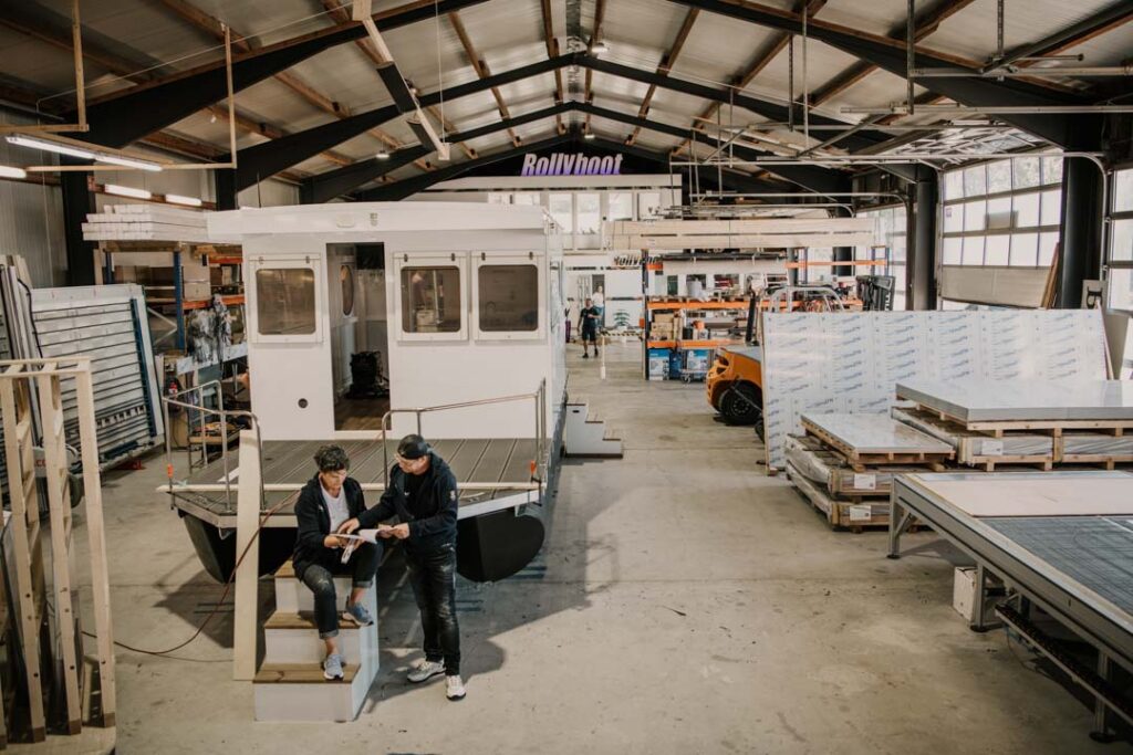 Marion Hanisch und Roland Delater, Gründer und CEOs von Rollyboat, besprechen einen Bauplan am Bug eines Hausboots in der Werkshalle in Brandenburg, Unternehmensfotografie