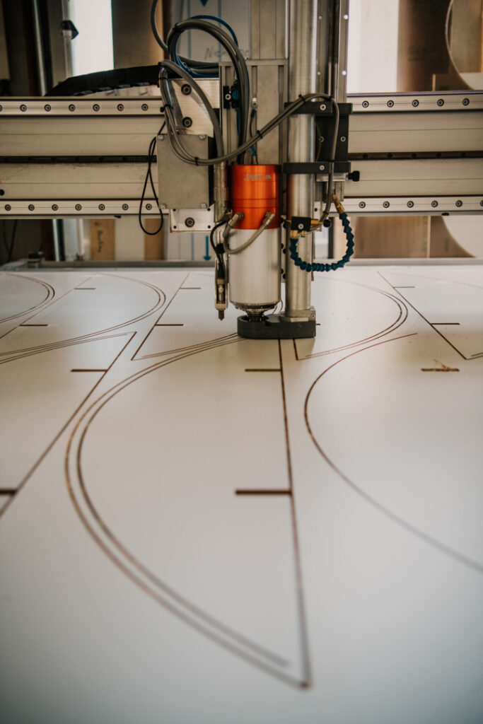 Detailaufnahme einer CNC-Fräse, die Bauteile aus einer Alu-Dibond-Platte fräst, Unternehmensfotografie