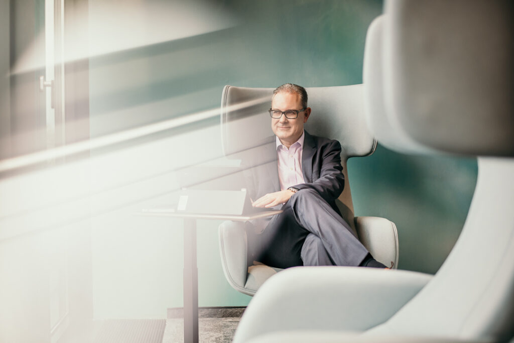 Manager der Santander Bank sitzt im Sessel und arbeitet am Tablet in grünlichem Raum – authentisches Businessportrait von Businessfotograf Hamburg