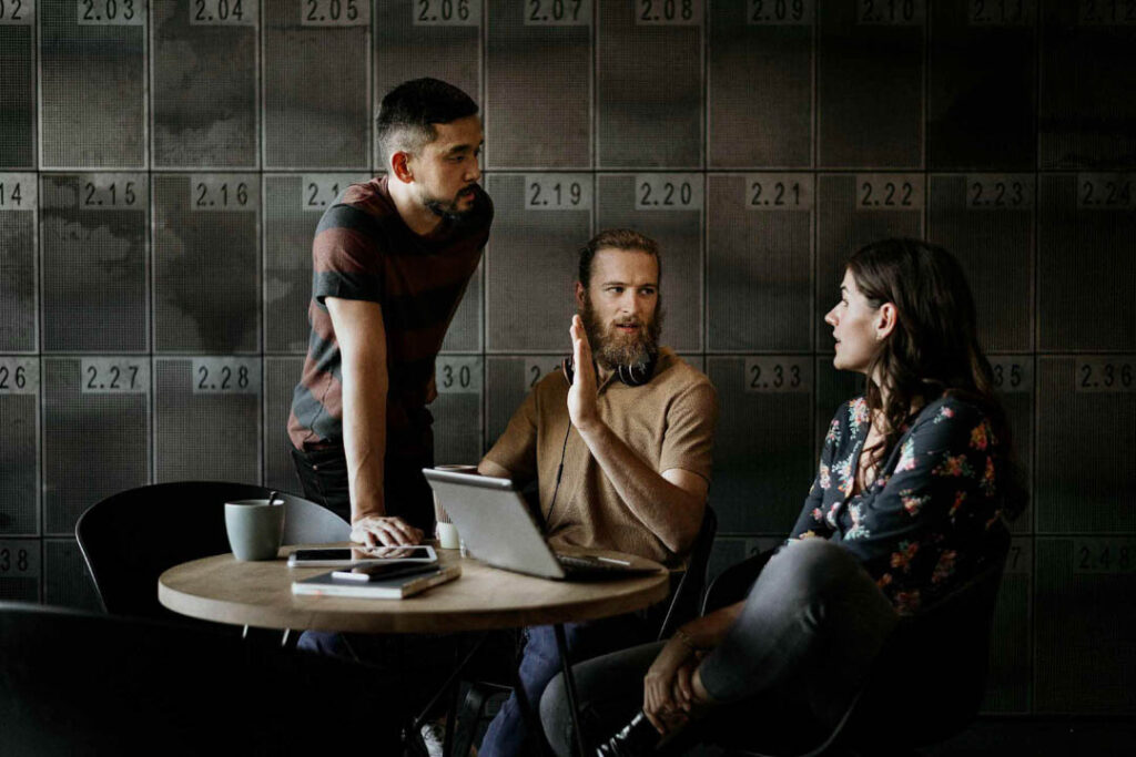 Junge, hippe Office-Mitarbeiter halten ein Meeting in dunklem Umfeld vor metallischen Spinden, Businessfotografie für Siemens