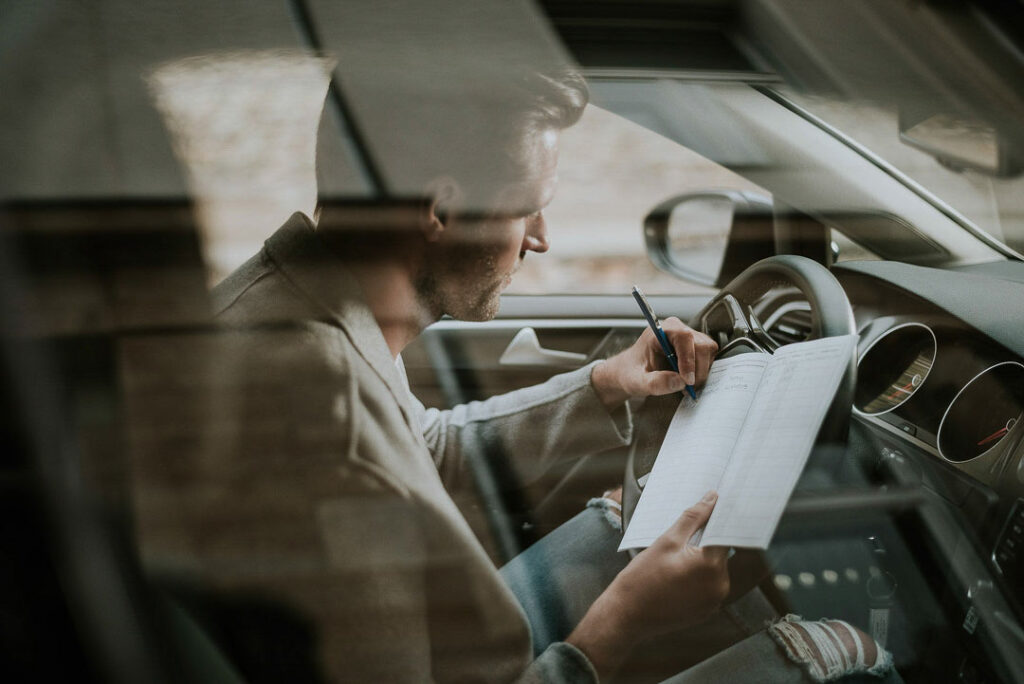 Authentische Corporatefotografie zeigt einen Geschäftsmann am Steuer eines Volkswagen, aufgenommen durch die Fensterscheibe mit Spiegelungen. Die Szene vermittelt Professionalität, Mobilität und die hochwertige Markeninszenierung für Volkswagen Financial Services.