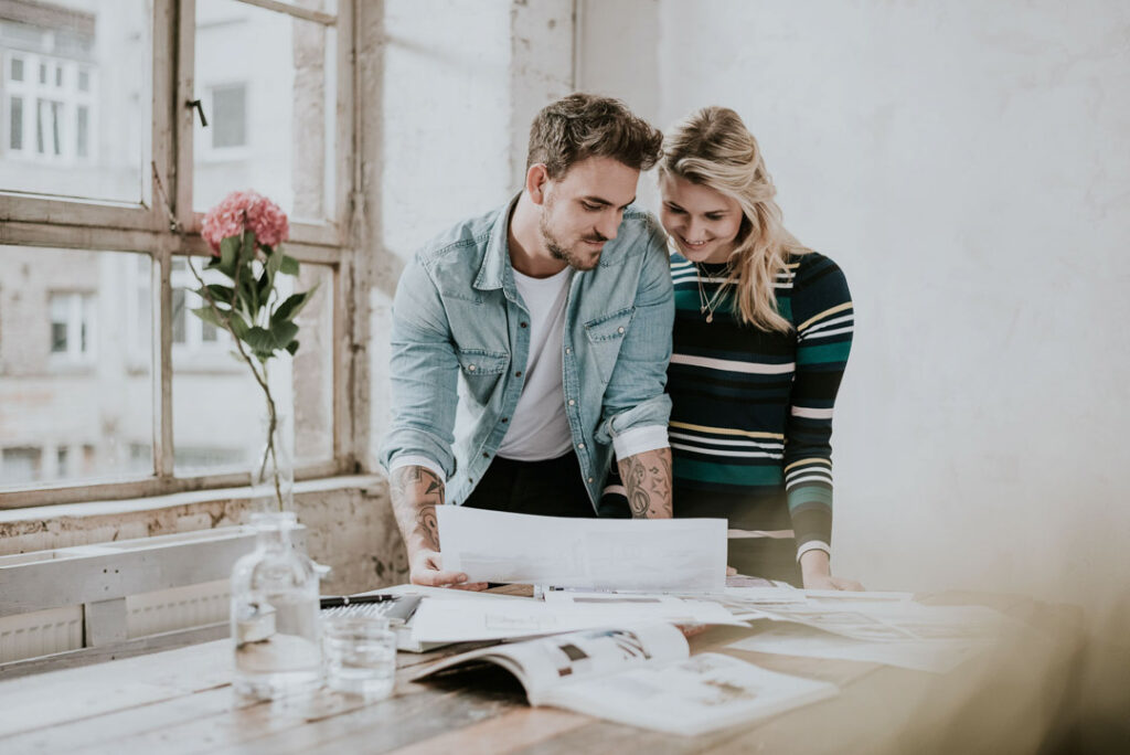 Glückliches Paar in einem Shabby-Chic-Office in Berlin betrachtet Bauunterlagen für die Planung ihres Hauses – Businessfotografie.