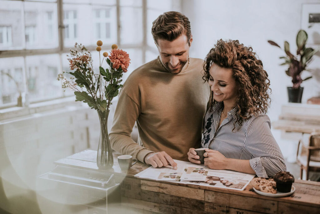 Paar betrachtet gemeinsam Bauunterlagen auf dem Tresen eines Cafés, aufgenommen von einem businessfotograf für Volkswagen Financial Services.