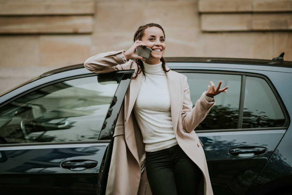 Modell Domitila Barros spielt eine Businessfrau, die an ihrem Auto telefoniert, fotografiert für businessfotograf.