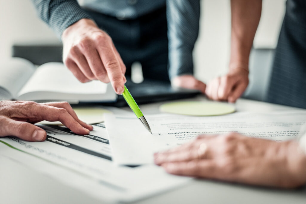 Nahaufnahme von Händen mit Stiften, Post-its und Büroaccessoires auf einem Tisch während eines Meetings – detailreiche Businessfotografie, die konzentriertes Arbeiten und kreative Zusammenarbeit zeigt.