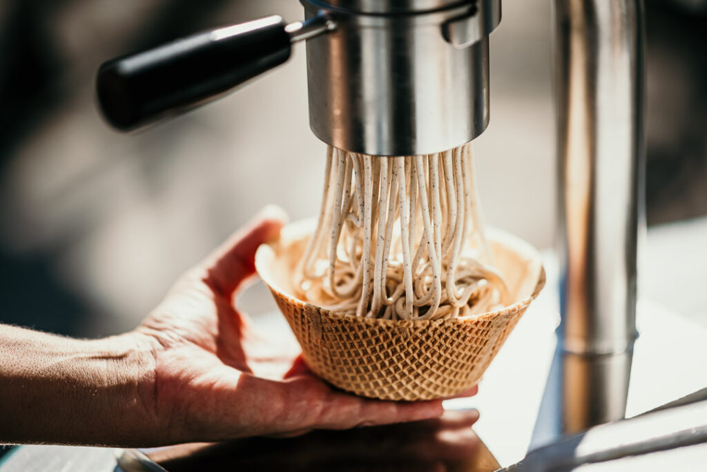 Close-up: Spaghetti-Eis wird frisch durch die Presse gedrückt, CEO der Manufaktur Kleine Eiszeit im Hintergrund, Foodfotografie