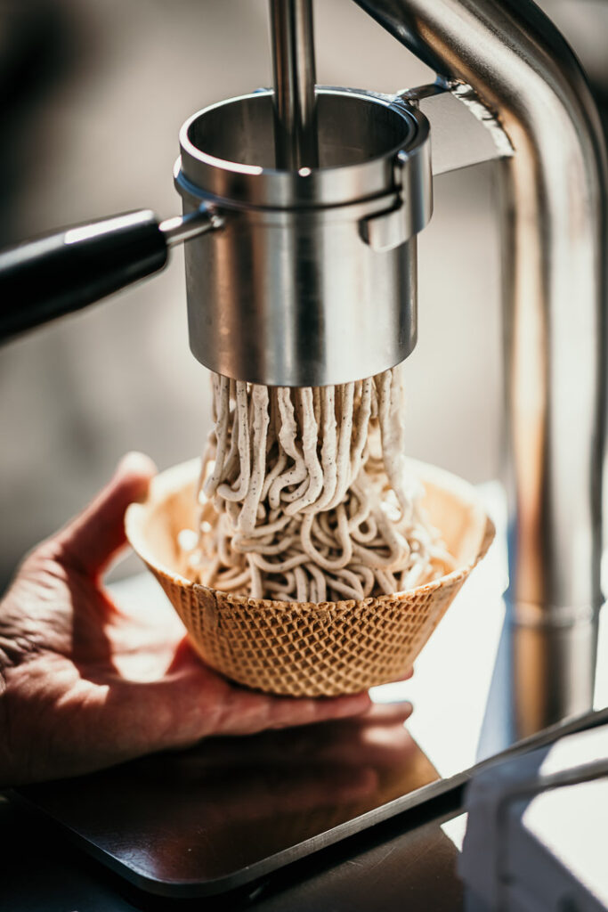 Close-up: Spaghetti-Eis wird frisch durch die Presse gedrückt, CEO der Manufaktur Kleine Eiszeit im Hintergrund, Foodfotografie