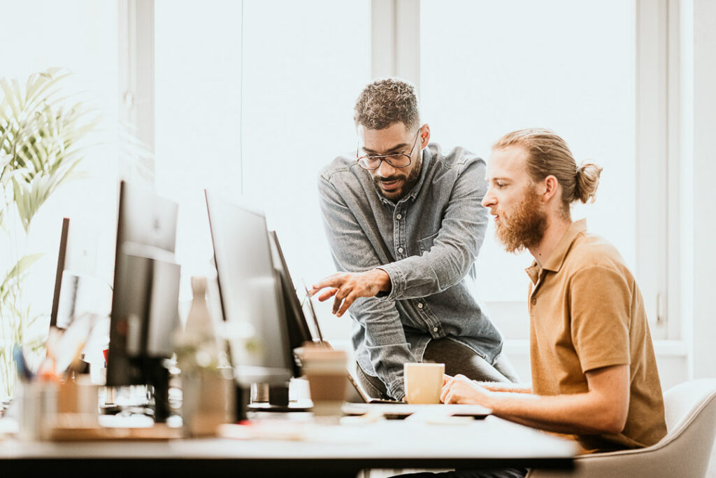 Office-Mitarbeiter besprechen sich an einem Computer mit mehreren Monitoren, Businessfotografie für Siemens