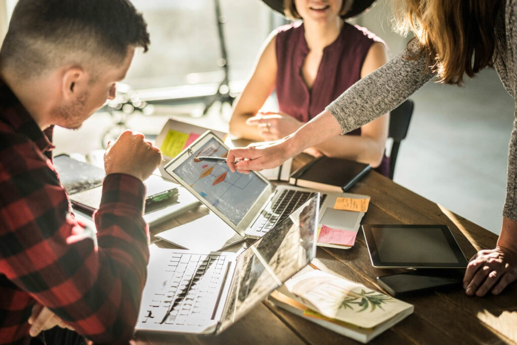 Drei junge Professionals führen ein Casual-Business-Meeting vor Spinden in moderner Co-Working-Atmosphäre – businessfoto.