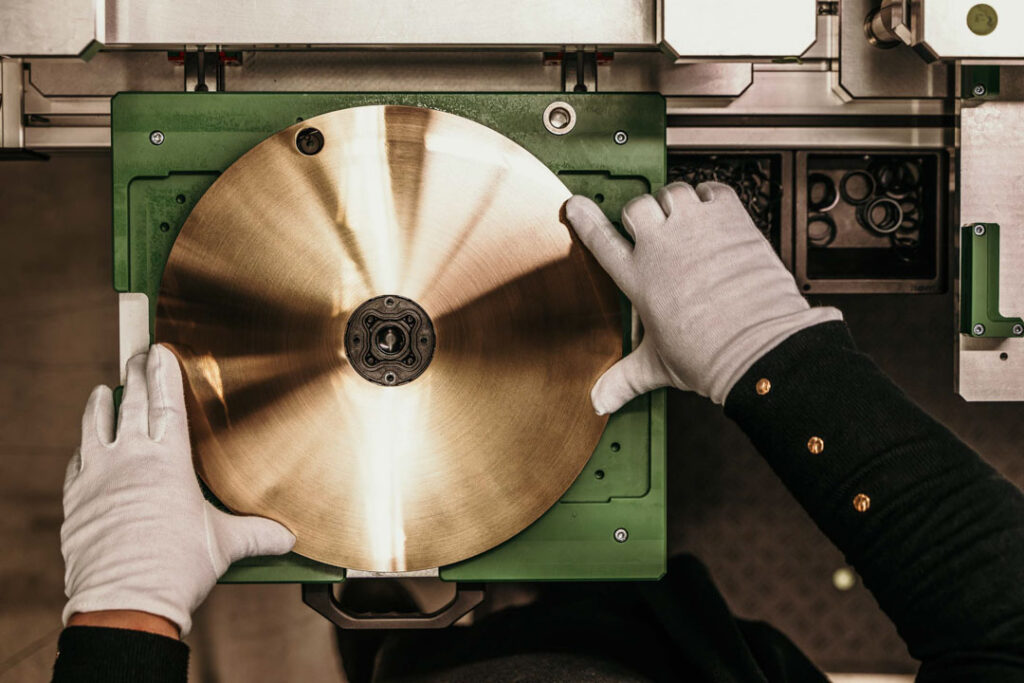 Hände in weißen Handschuhen setzen eine Hansgrohe Raindance Alive Kopfbrause in Brushed Bronze in die Fertigungstrasse ein, businessfotograf