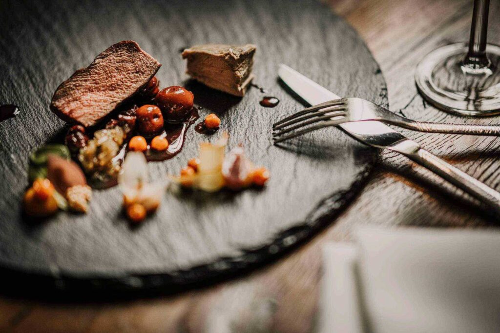 Branding Restaurants zeigt ein Gericht mit Hirsch, Sauce aus Kirschessig, Vogelbeeren und jungen Zwiebeln, zubereitet von Headchef Joerg Thiele im Restaurant Schloss Beuchow, Spreewald – stilvolle Food-Präsentation in historischem Ambiente