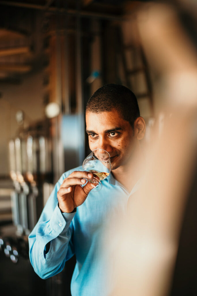 Foodfotograf zeigt einen Rum-Schnapsbrenner auf Mauritius, der die Qualität seiner Ware direkt an der Destille mit der Nase prüft – handwerkliche Spirituosenproduktion im Detail.