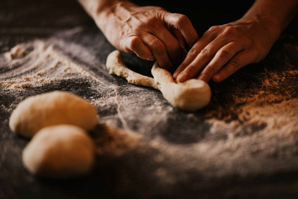 Restaurant photo zeigt Brezeln, die im Tempel74 Apartments in Mellau, Österreich, von Hand geformt werden – Close-up Food-Fotografie mit Fokus auf Handwerk und Teig.