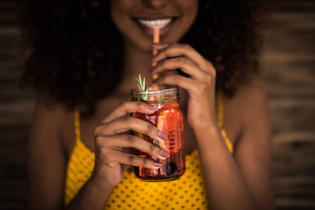 Foodfotograf zeigt ein Close-up eines lachenden Gesichts einer Afrikanerin, die einen kühlen Ice-Tea-Drink mit Strohhalm genießt – Location Inyoni Safari, Kapstadt, Südafrika