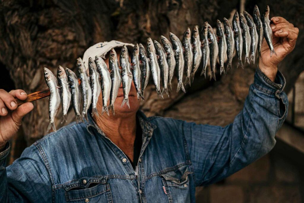 Restaurant Marketing Berlin zeigt einen Fischer in Kroatien, der Sardinen zum Räuchern aufreiht – traditionelle Fischzubereitung mit Foodbezug,