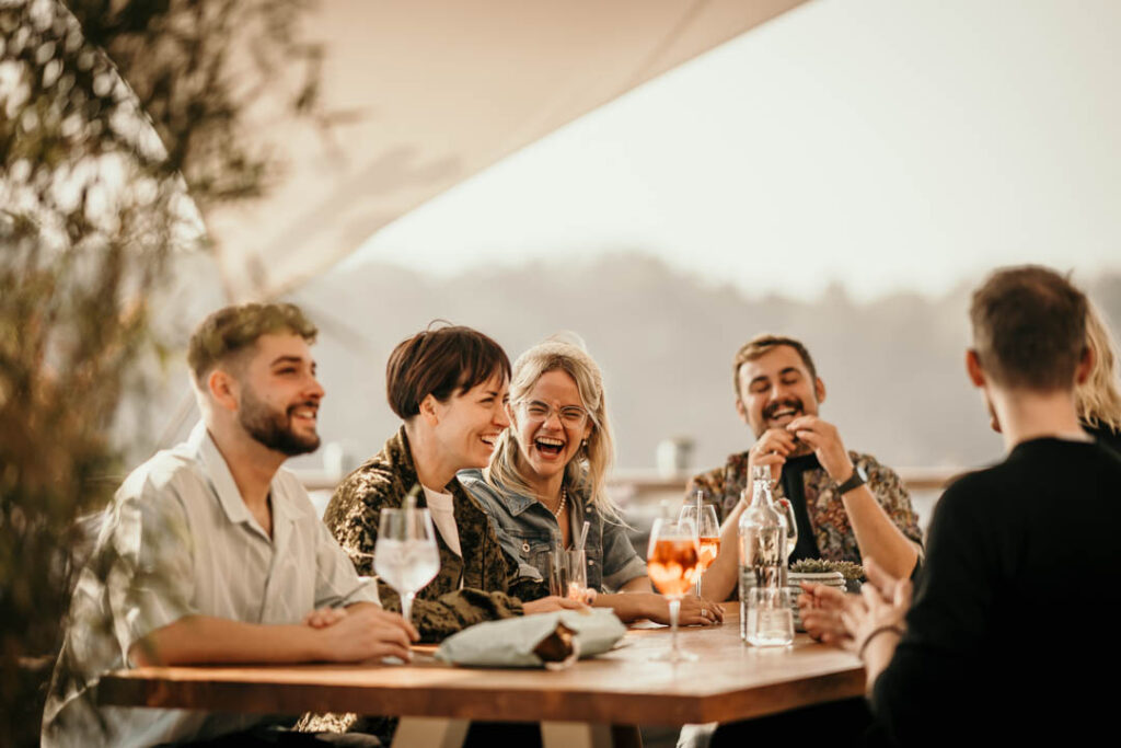 Gäste lachen und haben Spaß auf der Terrasse der Hafenküche Berlin – lebendige Outdoor-Hospitality-Fotografie für authentische Restaurantmomente.
