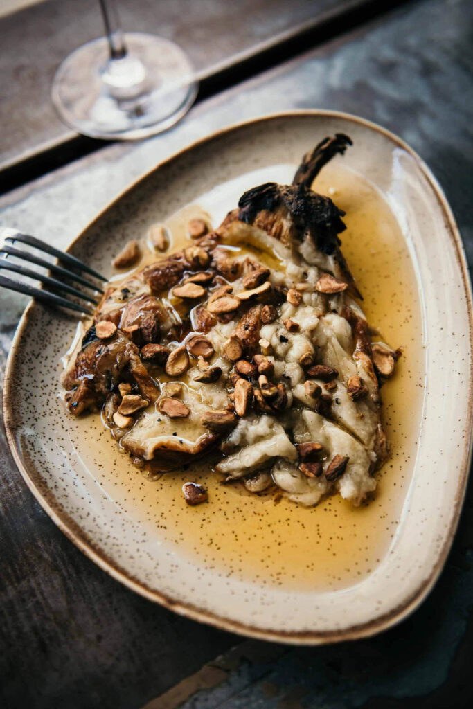 Restaurant Marketing Ideas zeigt Chef Mor Efrati und Restaurant Manager Liron Azulay im Restaurant/Bar Yudale auf dem Mahane Yehuda Markt in Jerusalem, Israel, mit einem Gericht aus Aubergine.