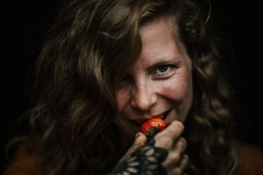 Foodfotograf hält Close-up-Portrait einer rothaarigen Frau fest, die genussvoll in eine frische Erdbeere beißt.