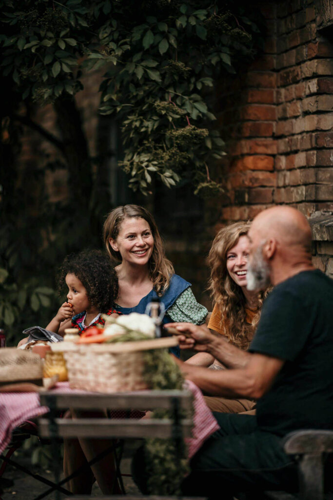 Food Fotografie zeigt eine Gruppe Biobauern, die am Esstisch sitzt und sich lachend unterhält – Foodfotograf fängt die authentische Stimmung ein, Food Fotograf inszeniert das natürliche Setting, Foodfotograf Hamburg und Foodfotograf Berlin dokumentieren die fröhliche Zusammenkunft.