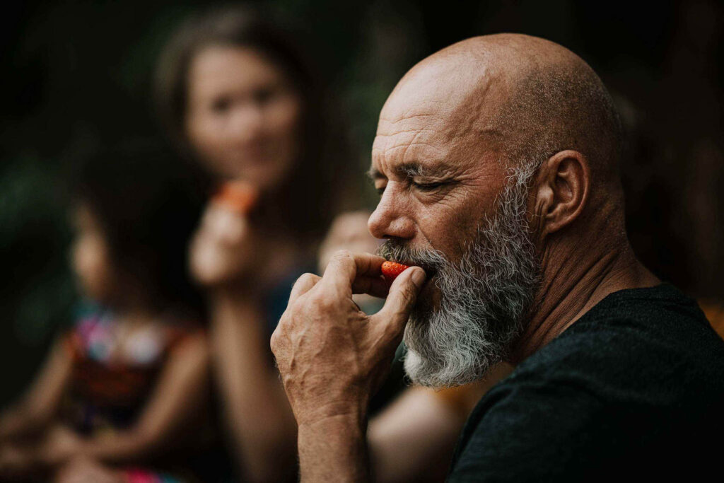 Food Fotografie zeigt einen Bestager-Biobauern im Portrait, der genüsslich in eine Erdbeere beißt – Foodfotograf hält den Moment fest, Food Fotograf inszeniert die natürliche Szene, Foodfotograf Hamburg und Foodfotograf Berlin dokumentieren die authentische Stimmung.