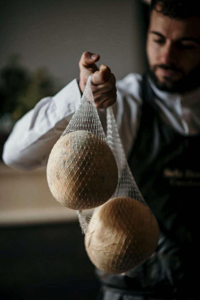 Foodfotograf zeigt einen Käser, der italienischen Käse in der Hand hält, um ihn lufttrocknen zu lassen – traditionelles Handwerk im Detail.