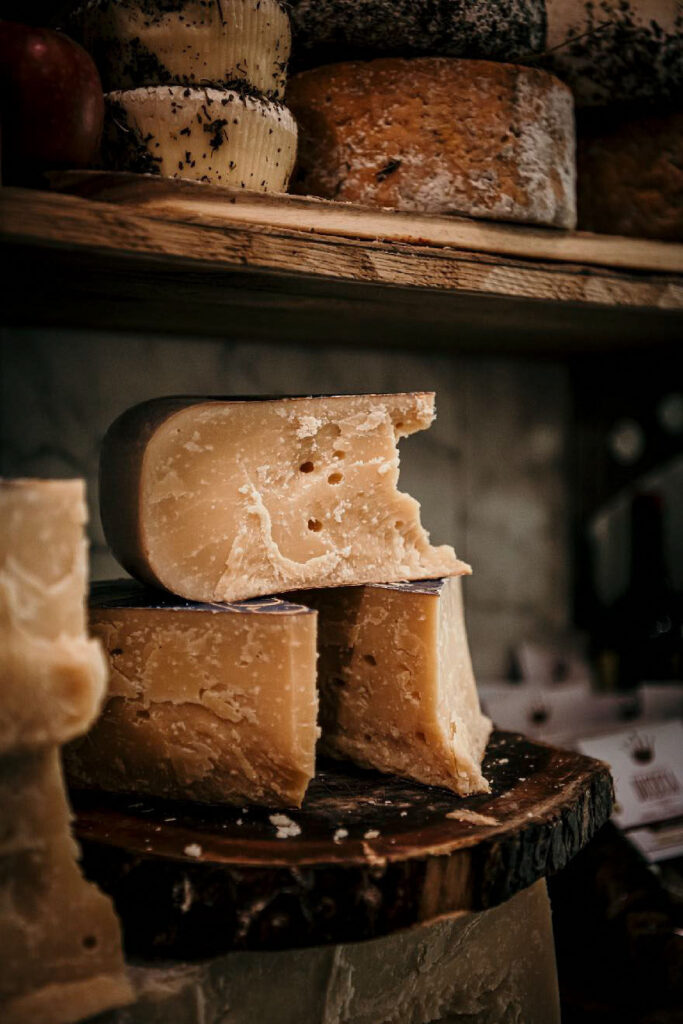 Food photography zeigt italienischen Hartkäse, gestapelt im Regal eines Käsespezialitätengeschäfts in Italien – frische Produkte im Detail.
