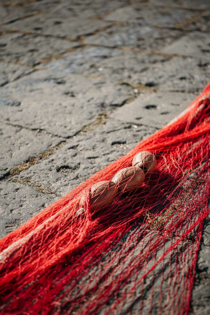 Gastronomie Consulting zeigt rote Fischernetze, die am Hafen von Catania repariert werden – Stillife mit Foodbezug und maritimer Atmosphäre.
