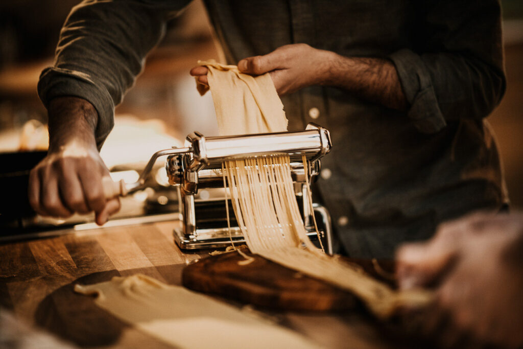 Foodfotograf zeigt ein Close-up, wie Nudeln in einer Pastamaschine selbst hergestellt werden – handwerkliches Kochen im Detail.