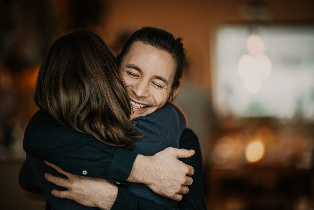 Food Fotograf zeigt ein Close-up-Portrait von Freunden, die sich umarmen – lachend und innig beim Abendessen.