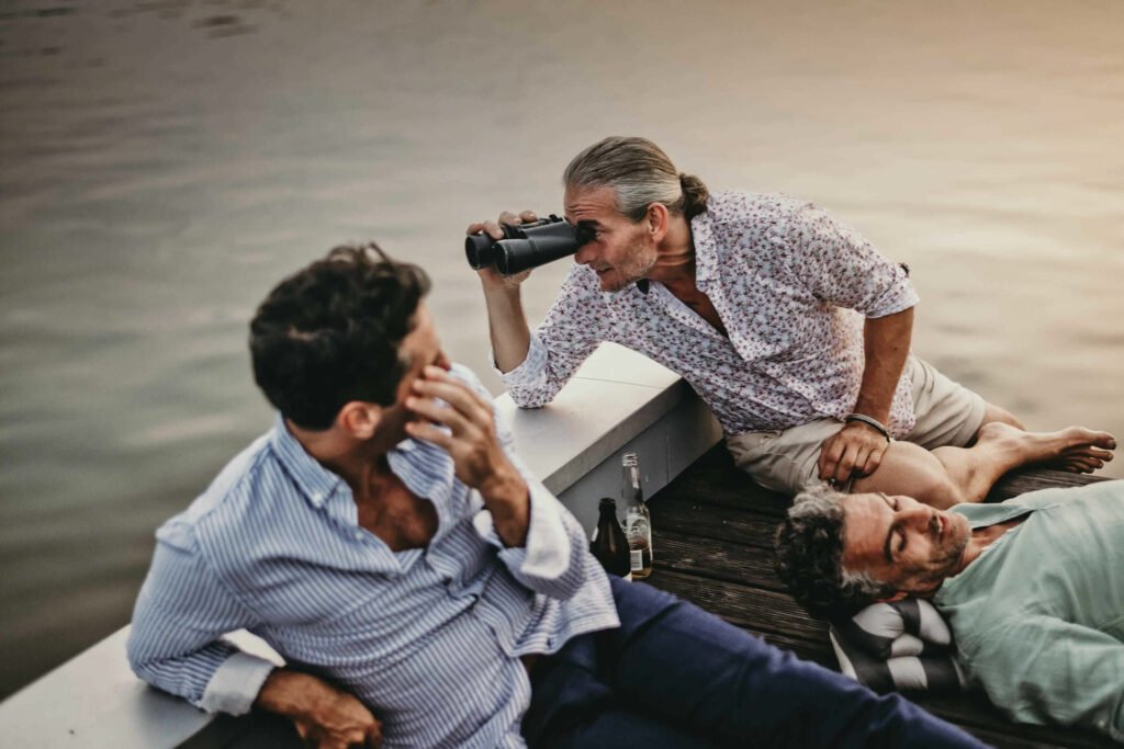 Food Fotografie zeigt Bestager-Freunde auf dem Dach eines Hausbootes, wie sie durch ein Fernglas schauen – fröhlicher Moment in entspannter Atmosphäre.