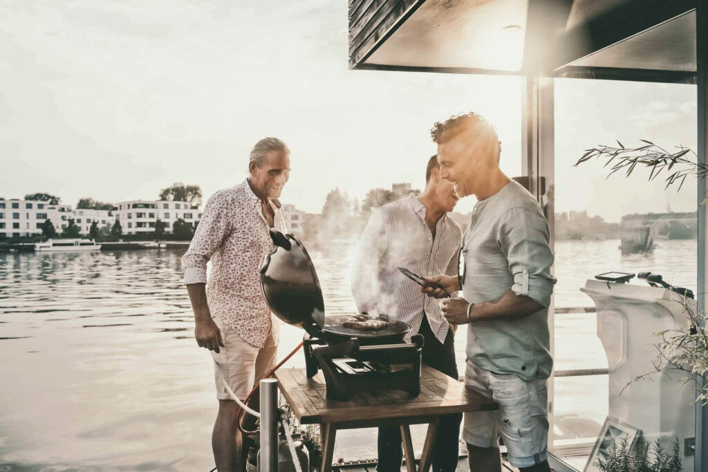 Foodfotograf Berlin zeigt Bestager-Freunde, die auf der Terrasse eines Hausbootes in Berlin grillen – entspannter Werbestyle-Moment., Webergrill.