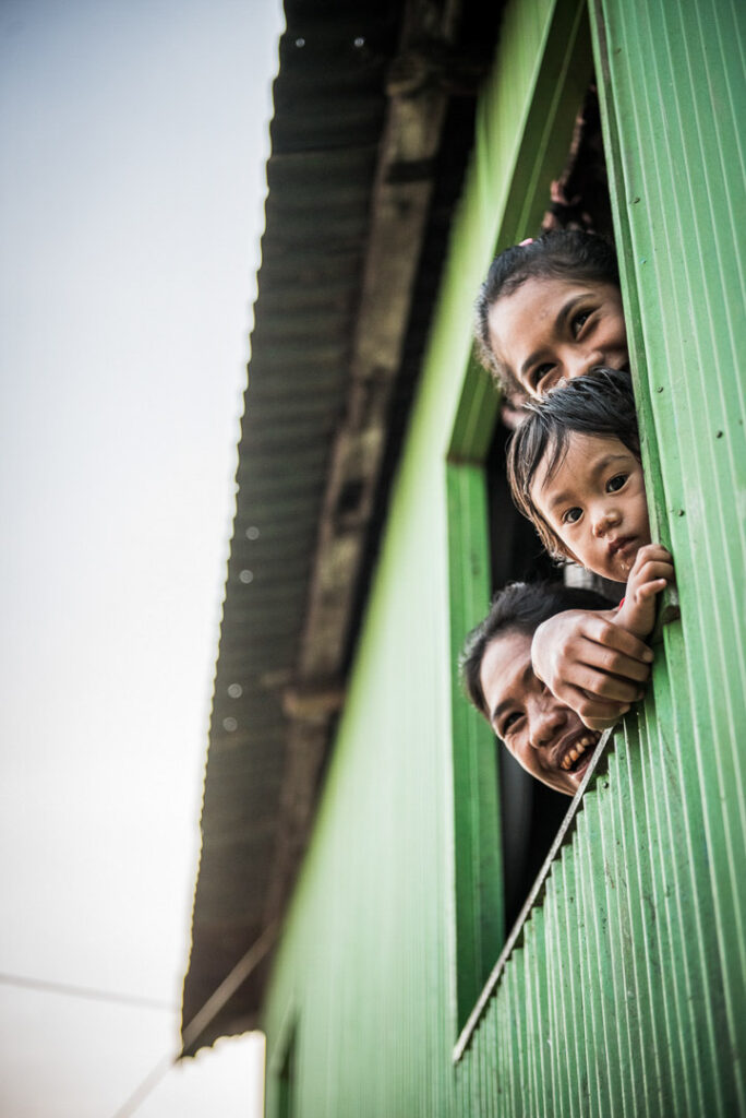 Einheimische Indonesier lachen aus dem Fenster ihres Hauses, authentische Momentaufnahme für die Amanikan Serie von Aman Hotels und Lufthansa, professionell fotografiert von einem Hotelfotograf.