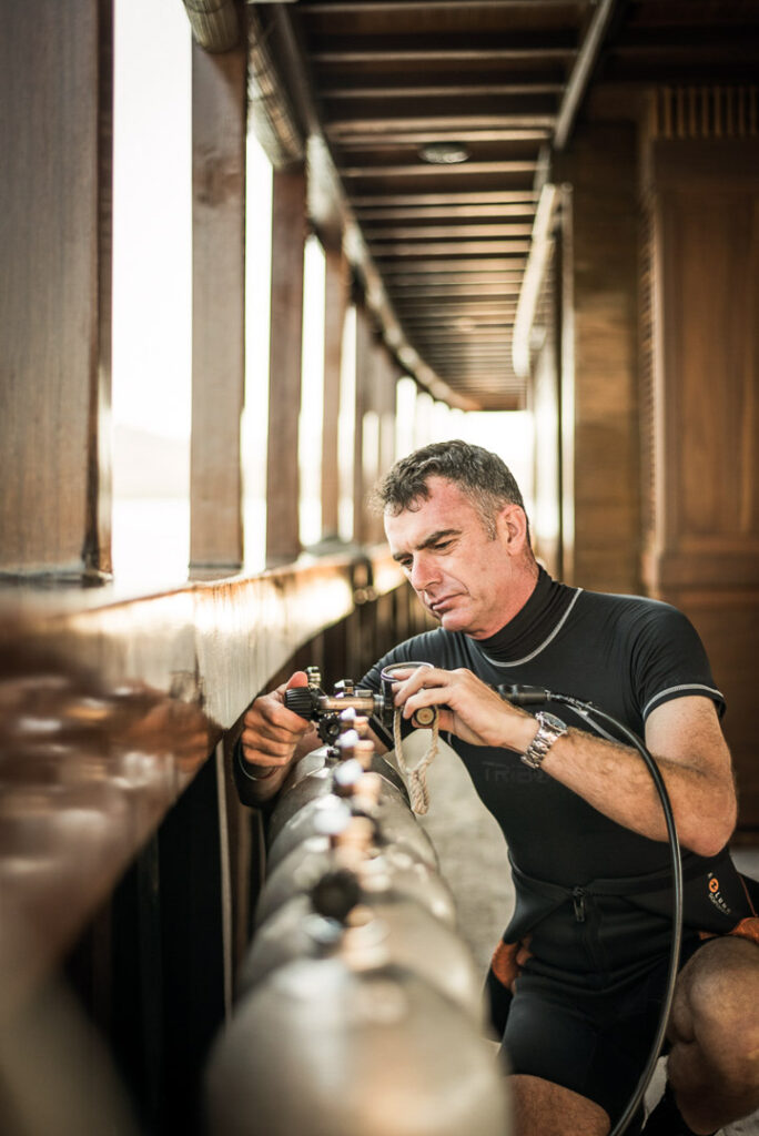 Privater Taucher und Guide prüft Druckflaschen an Bord der Amanikan – Hotelfotografie, Luxus-Reiseerlebnis.