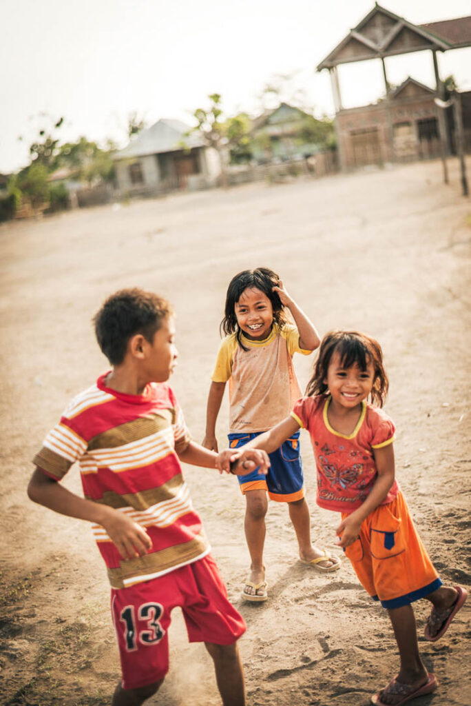 Einheimische Kinder spielen fröhlich vor dem Amanwana Resort, stimmungsvolle Hotelfotografie für Amanikan und Lufthansa, festgehalten von einem Hospitality Fotograf.