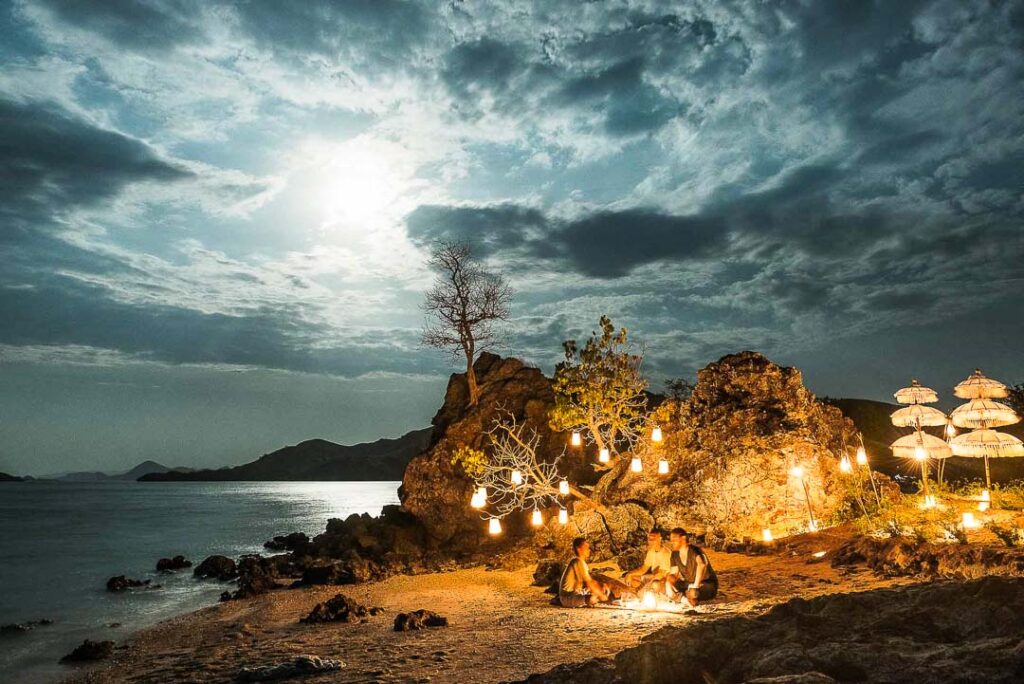 Nächtliches Full-Moon-Picknick luxuriös arrangiert auf einer Insel am Strand, Amanikan Crew serviert für Gäste, stilvolle Hotel-Visuals für Aman Hotels und Lufthansa aufgenommen von einem Hotel Marketing Fotograf.