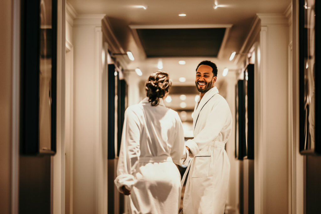 Paar läuft lachend im Bademantel den Hotelflur im Sofitel entlang – Hotelfoto für Hospitality-Marketing