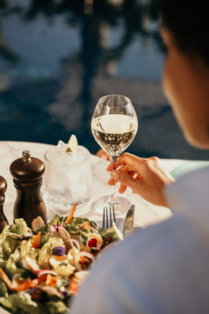 Weibliche Hand hält Champagnerglas neben Salat auf Tisch am Sofitel-Pool – Food-Close-up für Hotelfotografie und Hospitality-Marketing