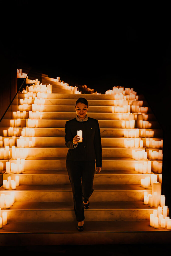 Hotelmitarbeiterin läuft mit brennender Kerze auf der Treppe voller Kerzen im Sofitel Hotel – stimmungsvolles Hotelfoto für Hospitality-Marketing