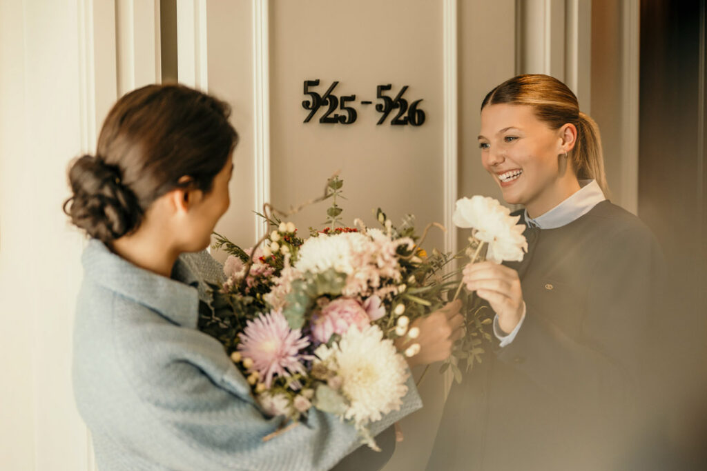 Concierge übergibt einem Gast an der Hotelzimmertür einen Blumenstrauß im Sofitel – Hotelfoto für Hospitality-Marketing