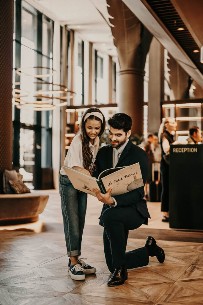 Concierge zeigt einem Kind im Sofitel-Hotelfoyer das Buch ‚Petit Prince‘ – Hotelfoto für Hospitality-Marketing