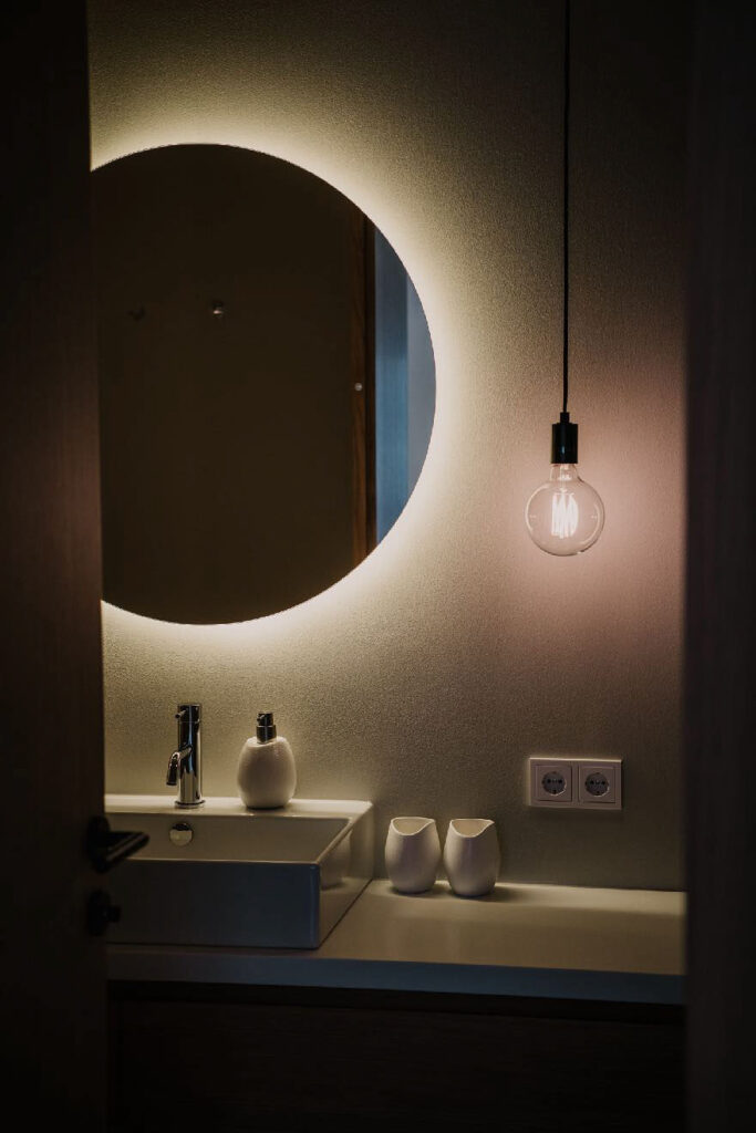 „Detailaufnahme beleuchteter Badezimmerspiegel mit Waschbecken und Armatur im Hotel Tempel74 – Architekturfotografie, modernes Hotelinterieur.“