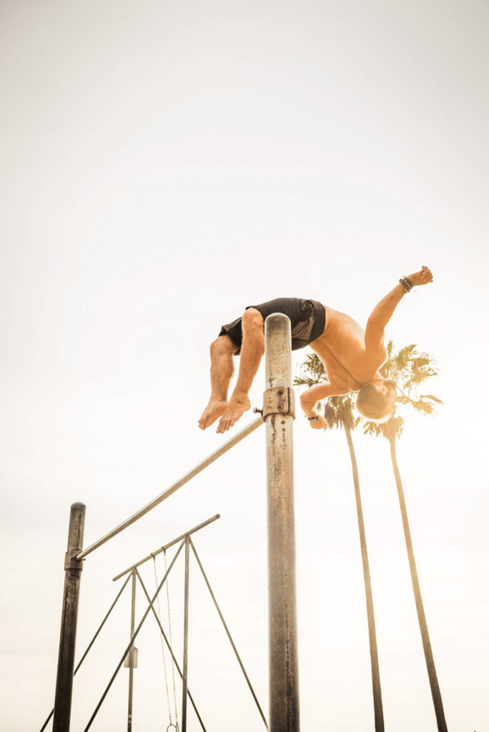Mann führt einen akrobatischen Sprung über ein Reck in einem Outdoor-Setting durch. Musclebeach, Losangeles, USA, fotografiert von Werbefotograf Berlin