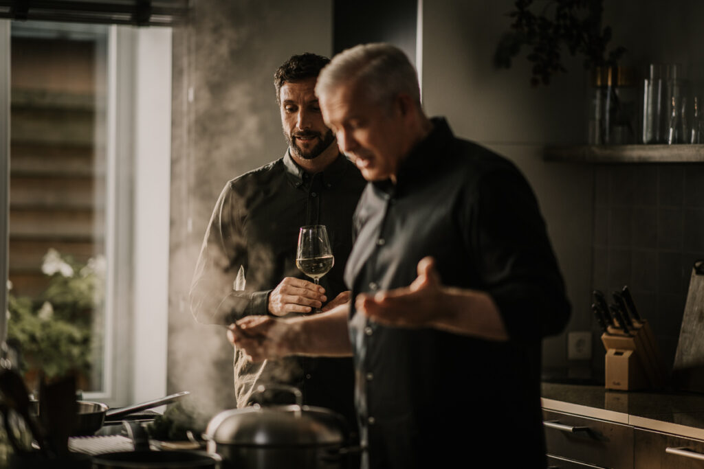 Alexander Herrmann erklärt einem Gast etwas beim Kochen in der Küche, authentischer Moment festgehalten von einem spezialisierten Foodfotografin.